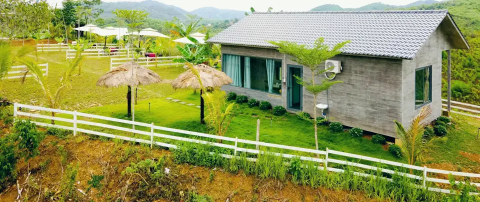 Bungalow mái ngói và sân cỏ rào trắng nhìn ra dãy đồi
